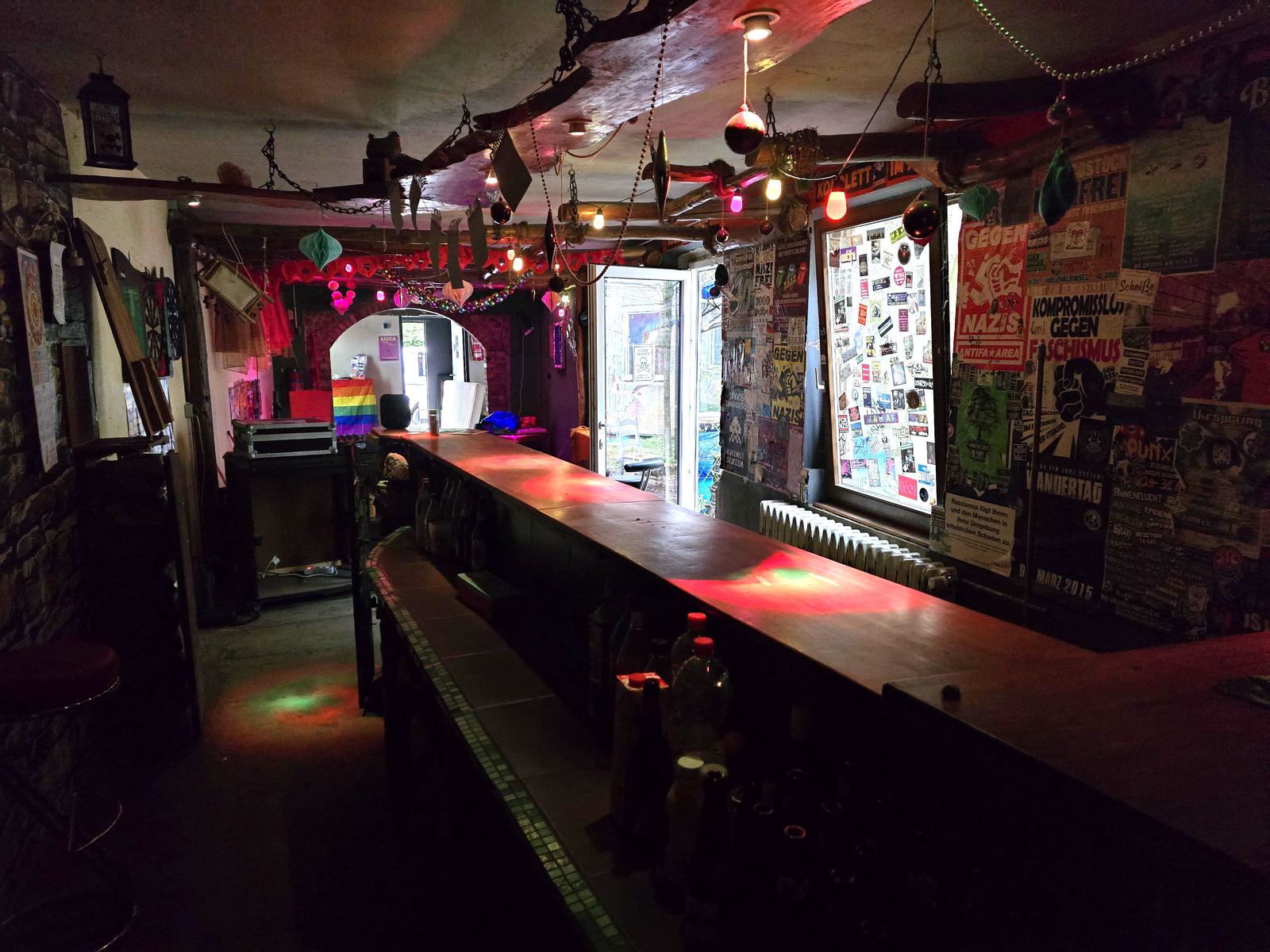 Die Bar im AJZ: lange Theke, bunte Lichter, Antifa-Poster und Sticker