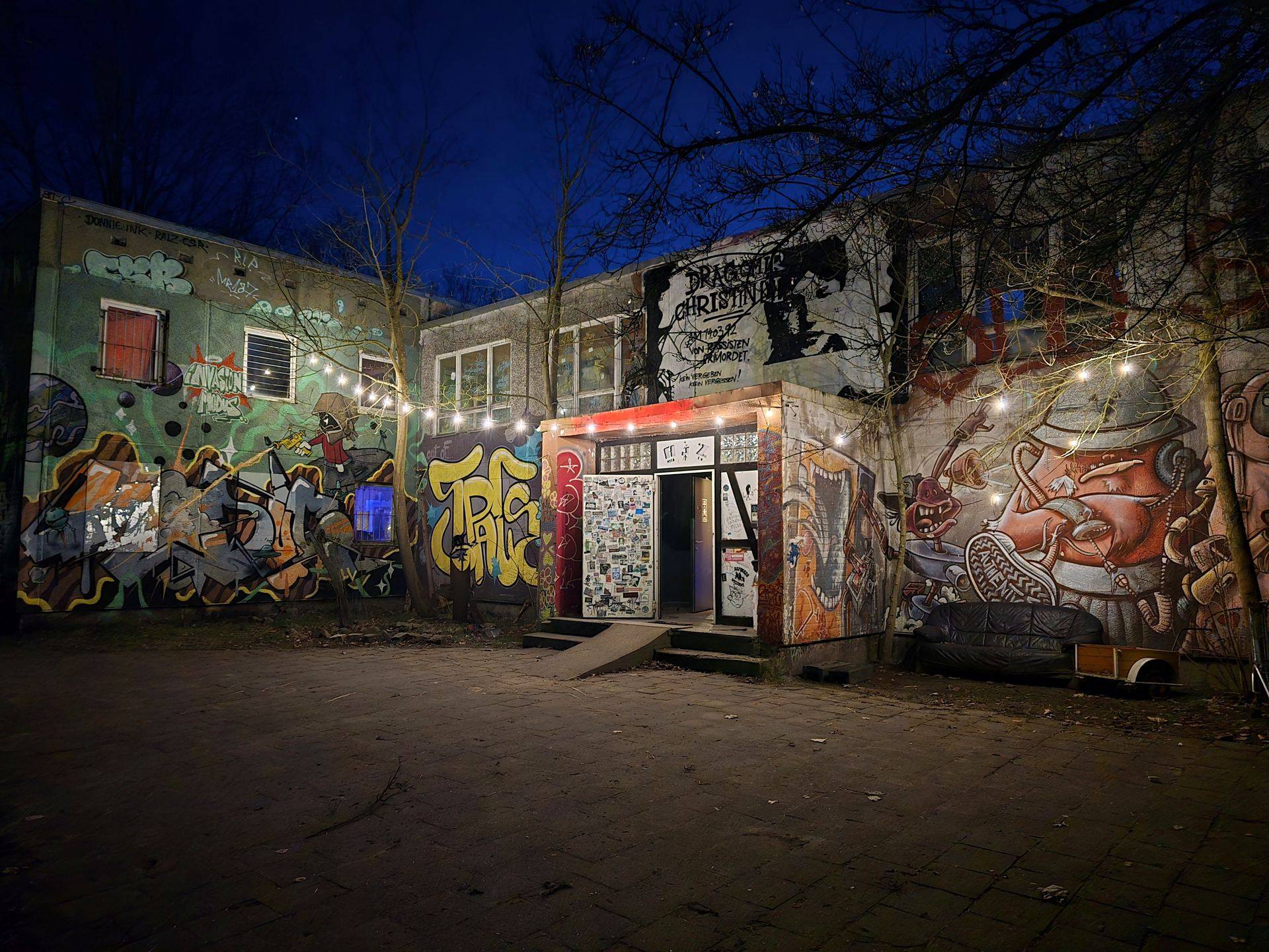 Das AJZ KITA bei Nacht: Graffiti-Fassade, Lichterkette über dem Eingang