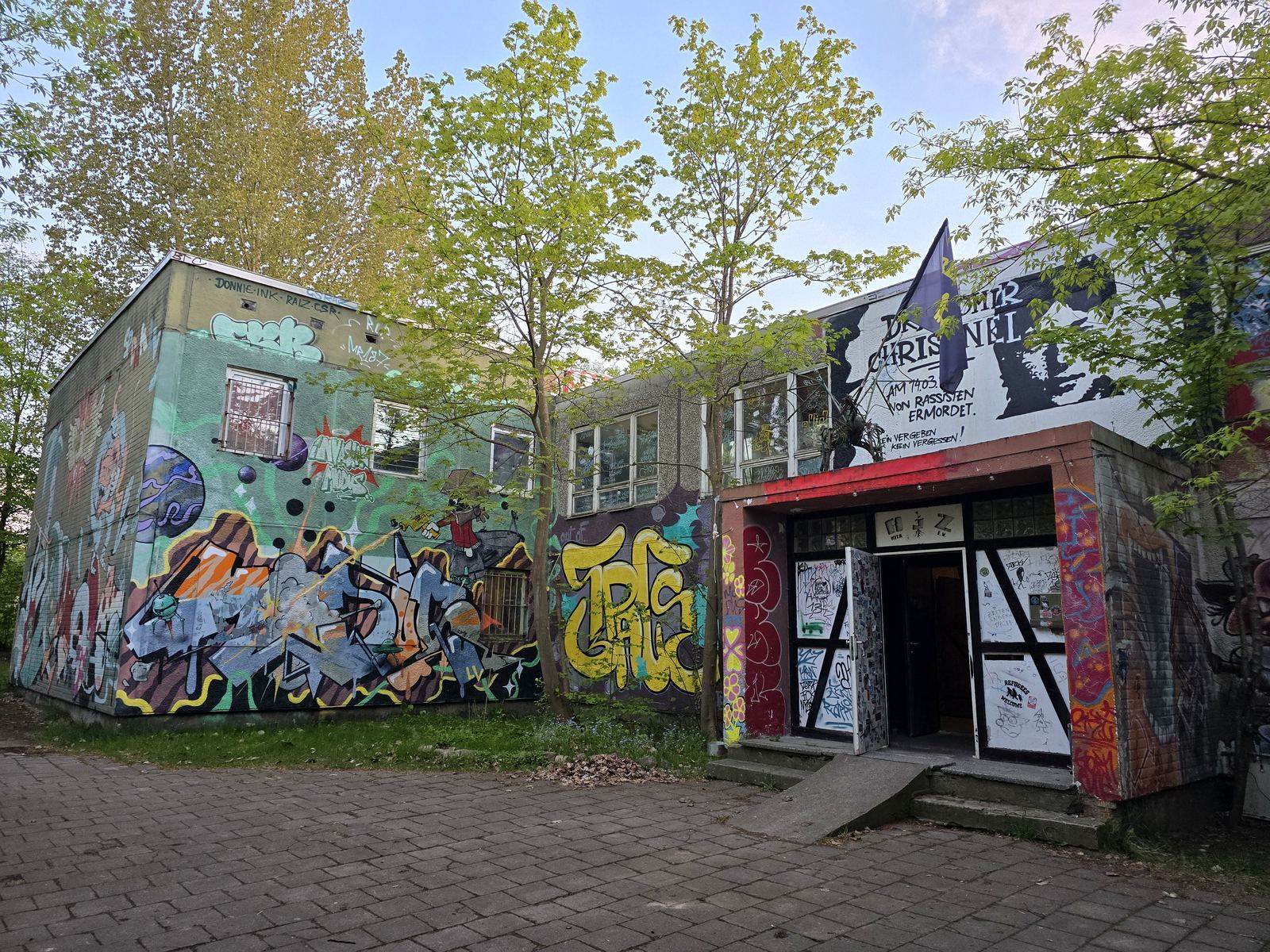 Das AJZ-Gebäude am Tag: komplett mit Graffiti bemalt, davor Bäume