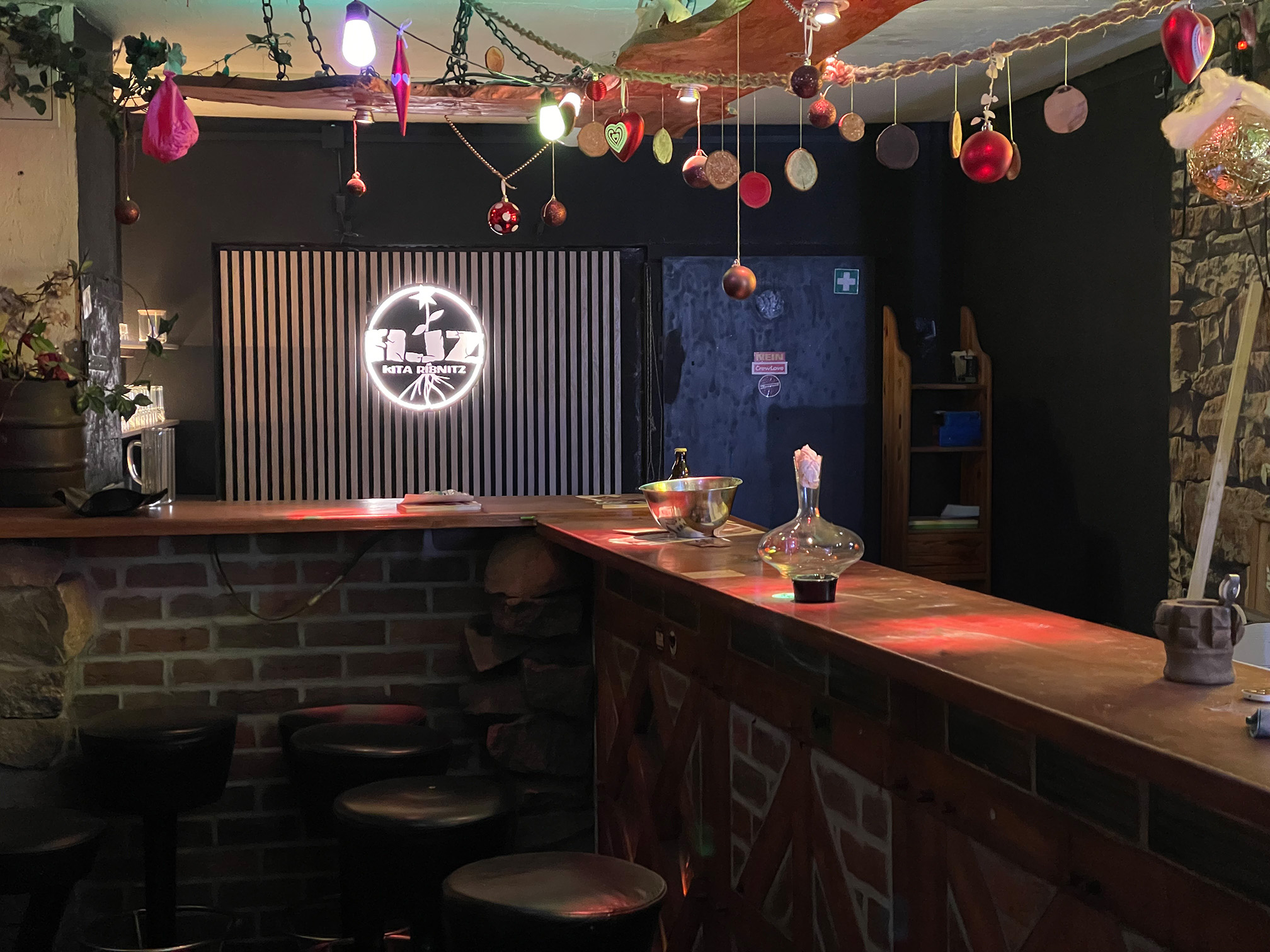 Die Bar im AJZ: lange Theke, bunte Lichter, Poster und Sticker an den Wänden